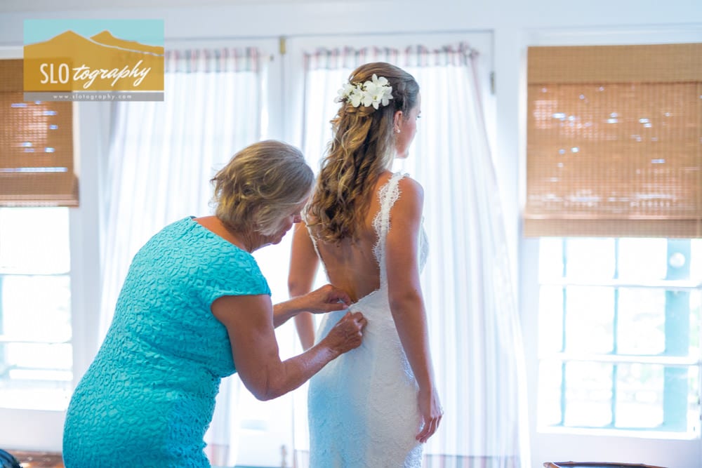 mom helps daughter button her wedding gown in well lit room