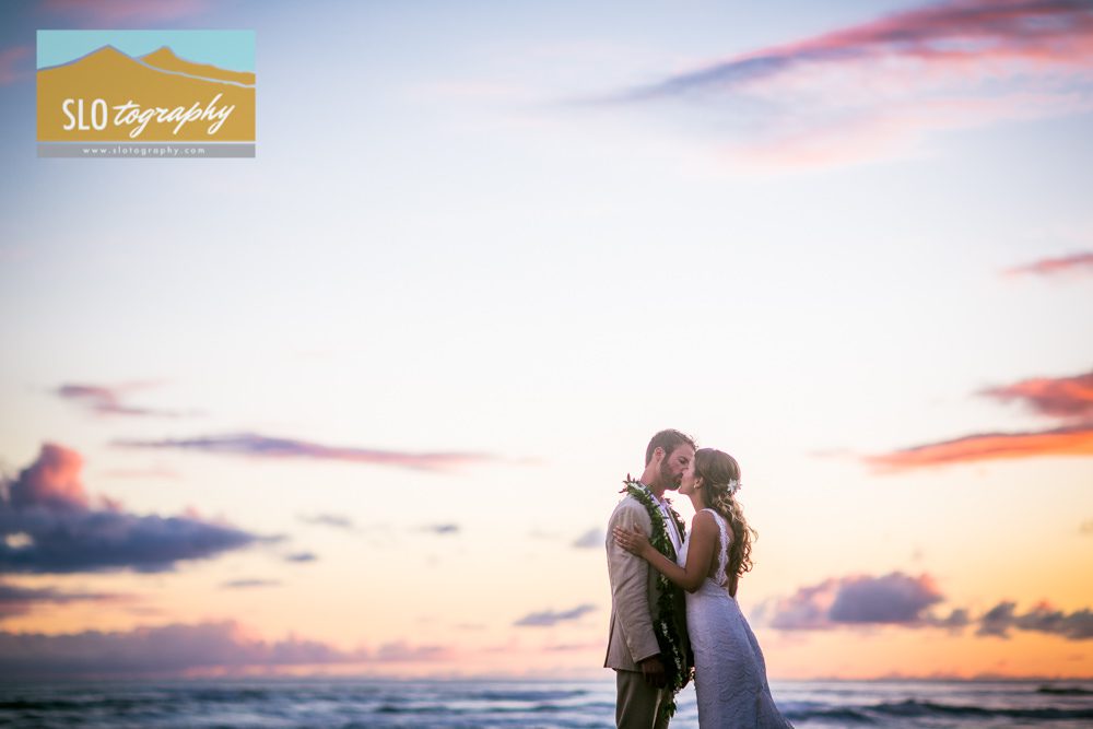newlyweds kiss at kauai sunset orange clouds